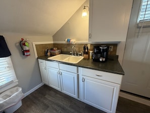A kitchen with white cabinets, a double sink, a coffee maker, and a fire extinguisher.