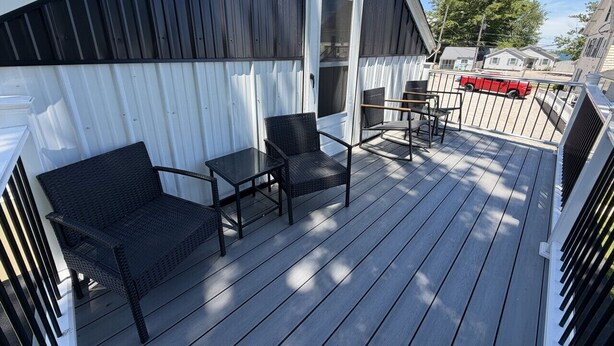A covered outdoor deck with a black wicker sofa, a small table, and a chair.