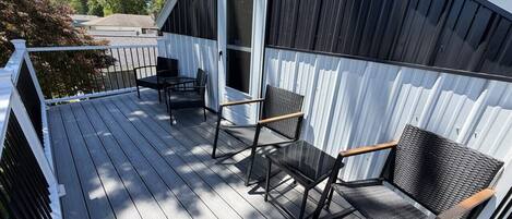 Eine überdachte Terrasse mit zwei Stühlen, einem Tisch, einer Tür zu einem Gebäude und einem weißen Geländer.