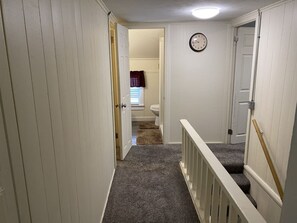 A narrow hallway with carpeted stairs leading to a bathroom with a toilet and a window.