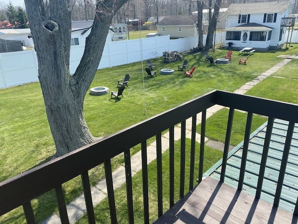 A backyard with a wooden deck, a tree, and a white fence.