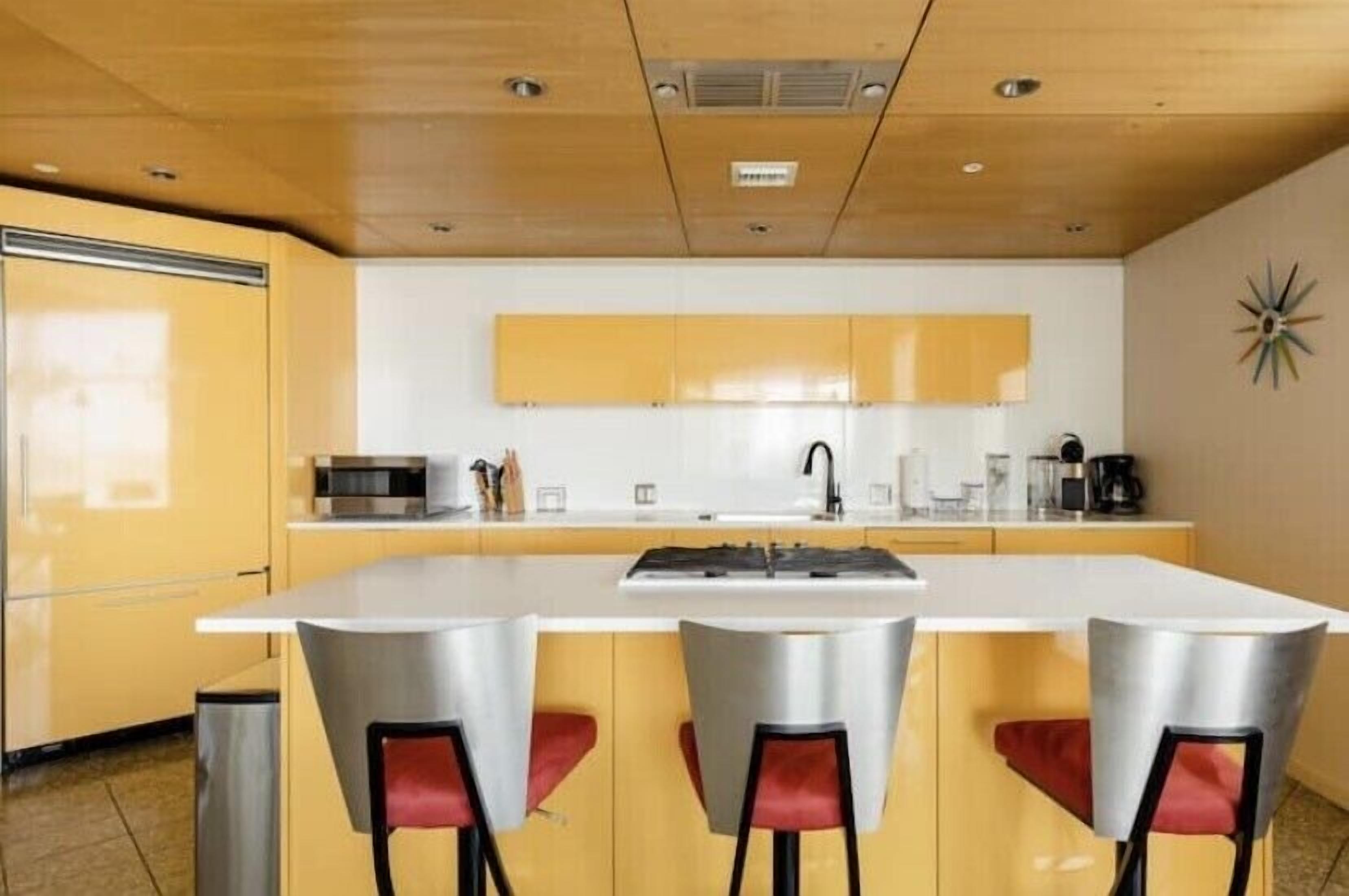 A modern kitchen with a central island, yellow cabinets, and red bar stools.
