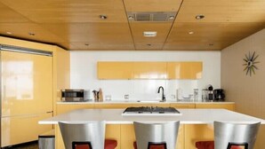 Een moderne keuken met een centraal eiland, gele kastjes en rode barstoelen.