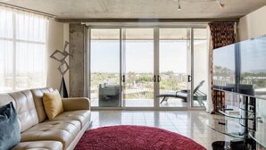Een moderne woonkamer met een leren bank, een rood vloerkleed en een grote televisie.