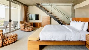 Een moderne slaapkamer met een groot bed, een televisie, een houten dressoir en een trap.