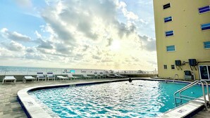 A swimming pool with a tiled edge, a metal ladder, and lounge chairs. - Beachfront condo with intracoastal views in Tampa Bay area, heated-cooled pool! (Indian Rocks Beach)