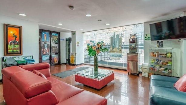 A modern lobby with red leather sofas, a glass coffee table, and a large window with a city view. - Hotel Budhha Resort (Bogotá)