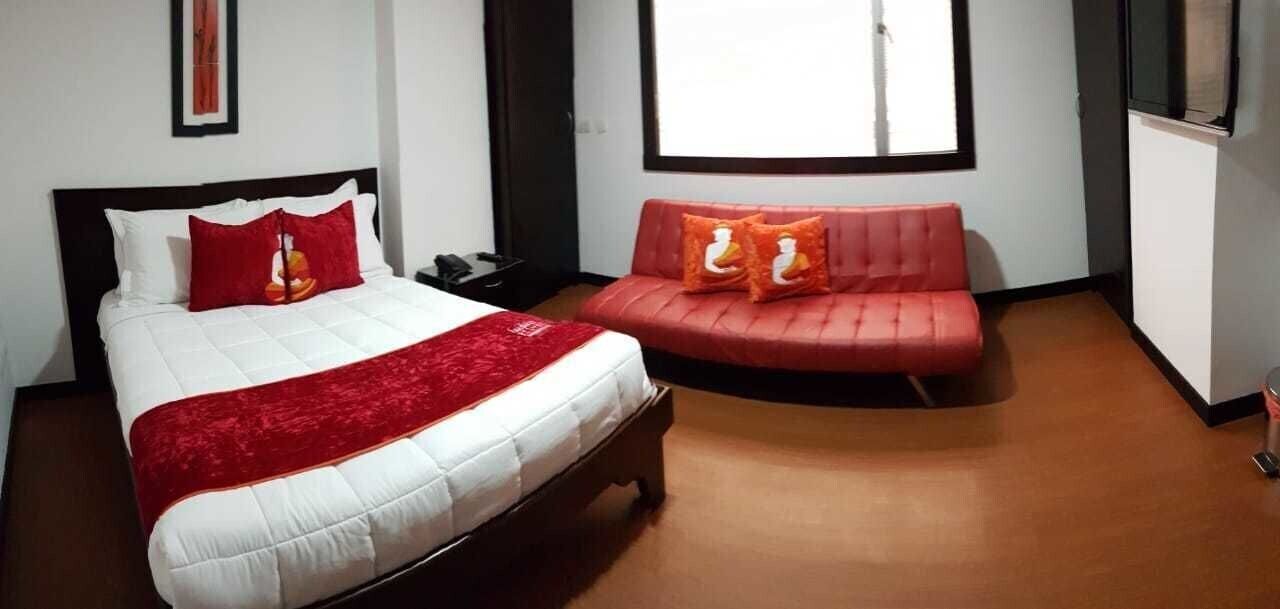 A hotel room with a bed, a red sofa, a window, and a television.