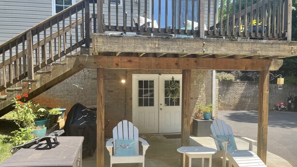 A covered outdoor seating area with two Adirondack chairs, a small table, and a wooden deck. - Travel Nurses (Madison Heights)