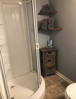 Divisória de chuveiro com porta de vidro, vaso sanitário e prateleira com toalhas dobradas.