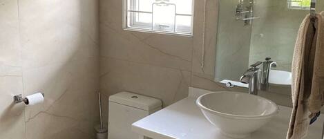 A bathroom with a toilet, sink, mirror, and a window with a blind.