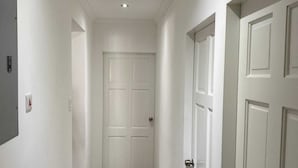 Un pasillo con paredes blancas, piso de madera y puertas blancas.