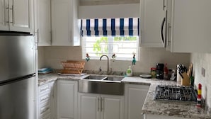 Una cocina con armarios blancos, un refrigerador de acero inoxidable, un lavamanos doble y una estufa a gas.