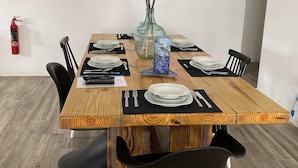 Un comedor con una mesa de madera dispuesta para cuatro, sillas negras, un florero con ramas de caña y un recipiente de vidrio azul.