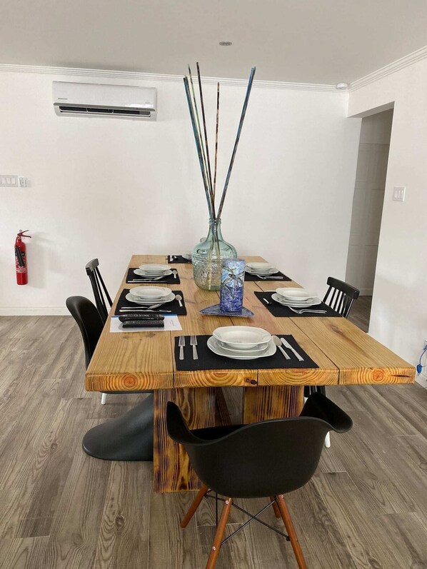 A dining area with a wooden table set for four, black chairs, a vase with reed sticks, and a blue glass container.