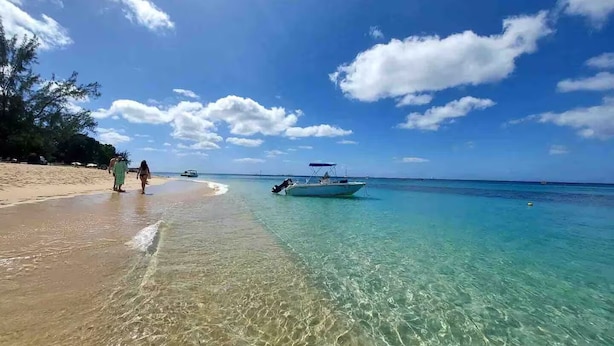 Una playa con agua turquesa cristalina, un bote y algunas personas caminando por la orilla.