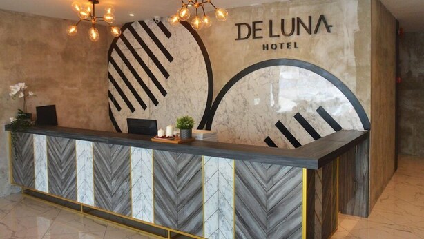 A reception desk at Deluna Hotel with a modern design, featuring a marble-patterned counter and a large, abstract wall art piece. - De Luna Hotel Sri Petaling (Kuala Lumpur)