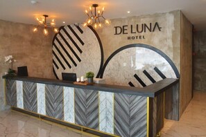 A reception desk at Deluna Hotel with a modern design, featuring a marble-patterned counter and a large, abstract wall art piece. - De Luna Hotel Sri Petaling (Kuala Lumpur)