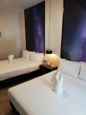 Une chambre d’hôtel avec deux lits simples, une table de chevet avec une lampe et une fresque murale représentant un ciel étoilé.