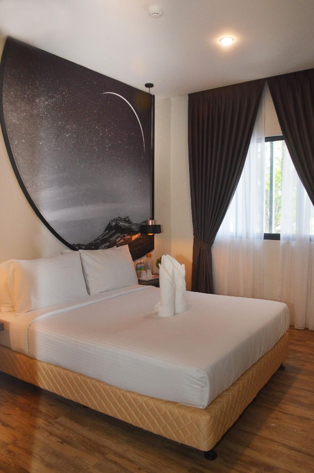 Une chambre d’hôtel avec un grand lit, une table de chevet, un téléviseur fixé au mur et une fenêtre avec des rideaux.