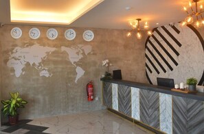 Un espace d’accueil comprenant une carte du monde, des horloges, un comptoir en marbre et un extincteur.