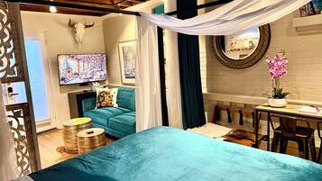 A cozy room with a teal bed, a television, a blue sofa, and a small table with a potted orchid.