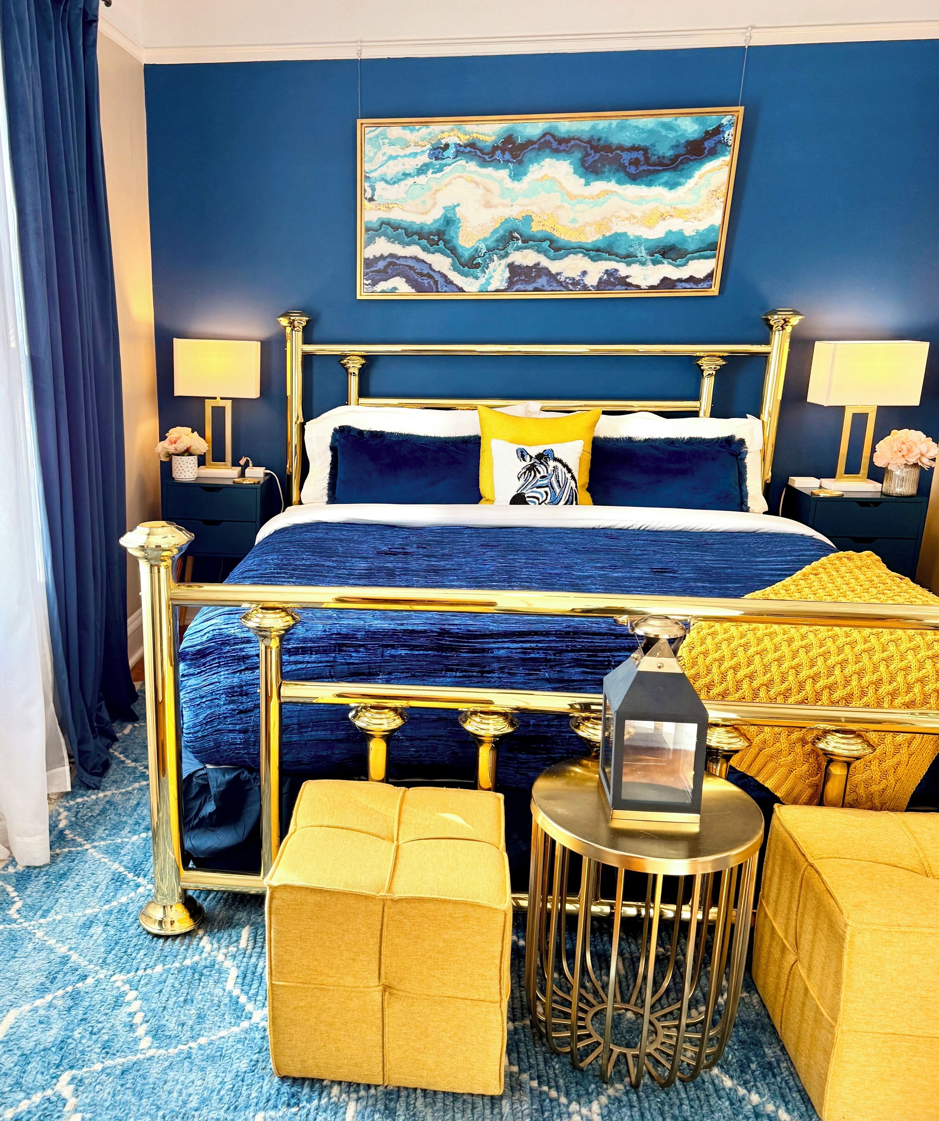 Een slaapkamer met een blauwe wand, een gouden bed, een schilderij en een blauw kamerkleed.