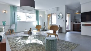 Una sala de estar moderna con una mesa redonda, dos sillones, un pequeño otoman y una lámpara colgante grande.