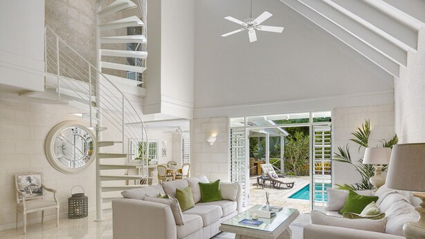 Ein großzügiger Wohnbereich mit weißer Treppe, Deckenventilator, Pool und Essbereich.