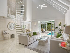 A spacious living area with a white staircase, a ceiling fan, a pool, and a dining area.