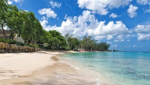 Ein Strand mit klarem türkisblauem Wasser, sandigem Ufer und üppigen, grünen Bäumen.