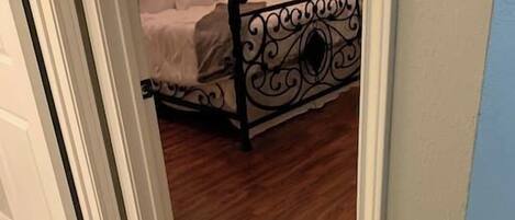 A bedroom with a bed, a nightstand, a lamp, and a measuring tape on the floor.