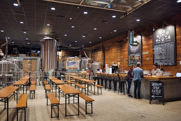 A brewery interior with stainless steel tanks, wooden tables, and a taproom sign.