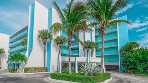 Un hotel moderno con varios pisos, palmeras y un cielo azul despejado.