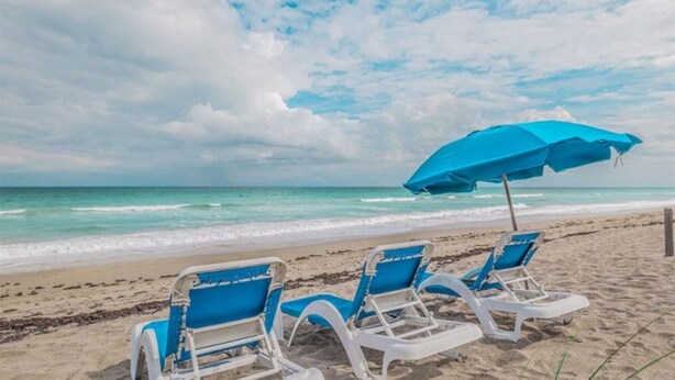 Una playa con dos sillas azules y una sombrilla azul.