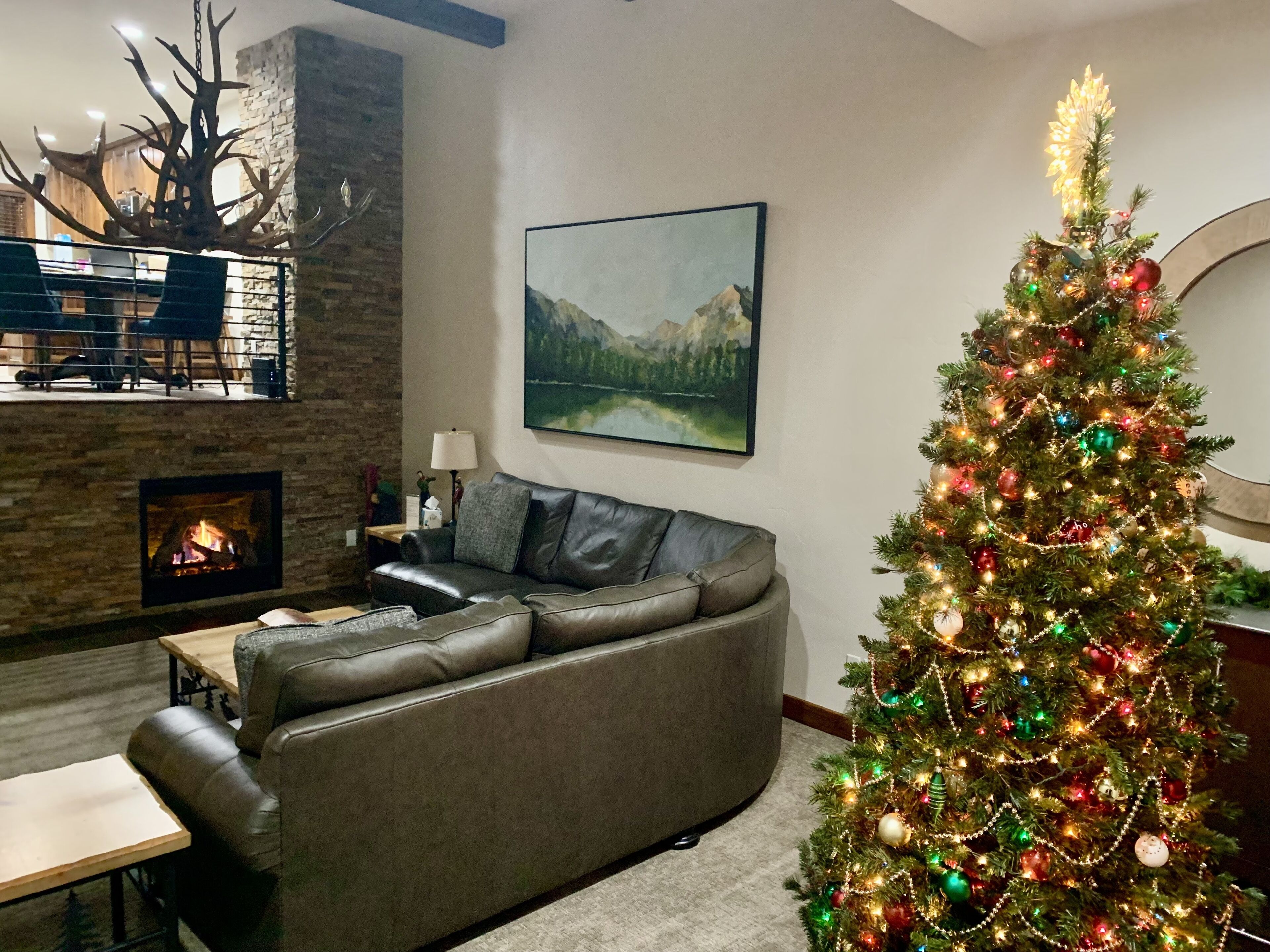 A cozy living room with a fireplace, a large sofa, a Christmas tree, and a painting on the wall.