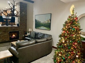 Un salon chaleureux avec une cheminée, un grand canapé, un sapin de Noël et un tableau accroché au mur.