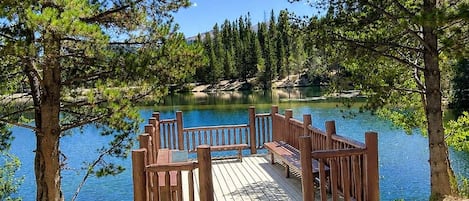 A wooden dock leading to a calm lake surrounded by pine trees.