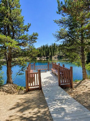 A wooden dock leading to a calm lake surrounded by pine trees.
