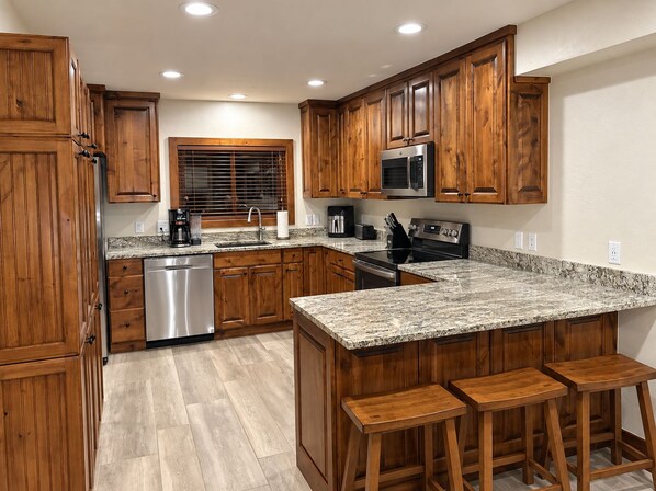 A kitchen with wooden cabinets, a granite countertop, a dishwasher, a microwave, and a stove.