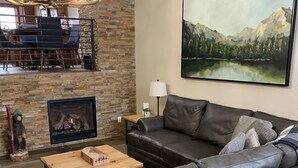 Ein gemütliches Wohnzimmer mit Kamin aus Stein, einer großen Couch, einem Holztisch und einer Kandelaber.