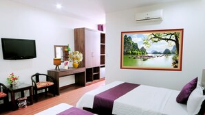 Een hotelkamer met twee bedden, een bureau met stoel, een televisie, een landschapschilderij en een airconditioner.