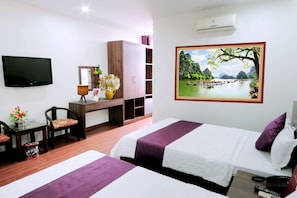 A hotel room with two beds, a desk with a chair, a TV, a painting of a landscape, and an air conditioning unit. - Van Giang Hotel (Ninh Binh)