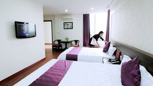 Een hotelkamer met twee bedden, een televisie, een bureau met stoel en een raam met gordijnen.