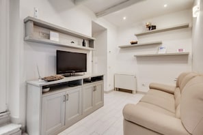 Una sala de estar moderna con un televisor de pantalla plana, armarios grises, un sofá beige y estantes empotrados con objetos decorativos.