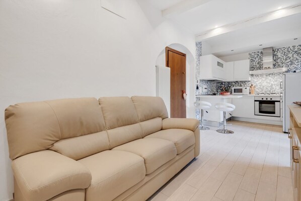 A beige sofa in a modern kitchen with white cabinets, a microwave, and a stove. - GuestHost - Coverciano Modern Apartment with Patio! (Firenze)