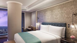A hotel room with a large bed, a desk, a chair, a nightstand, and a view of the city. - The Ritz-carlton Pune (Pune)
