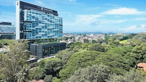 A modern hotel with a glass facade, surrounded by lush greenery and a clear view of the cityscape. - The Ritz-carlton Pune (Pune)