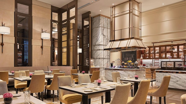 A hotel dining area with tables, chairs, and a kitchen in the background. - The Ritz-carlton Pune (Pune)