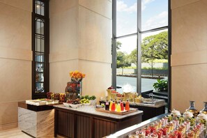 A buffet with various food items and beverages, a marble counter, and a view of a body of water through large windows.